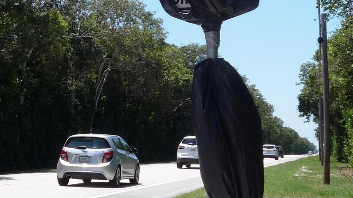 Plastic bags cover 55 mph speed-limit signs on County Road 905 in Key Largo after a construction dispute. The speed limit was lowered when work altered the width of the road.